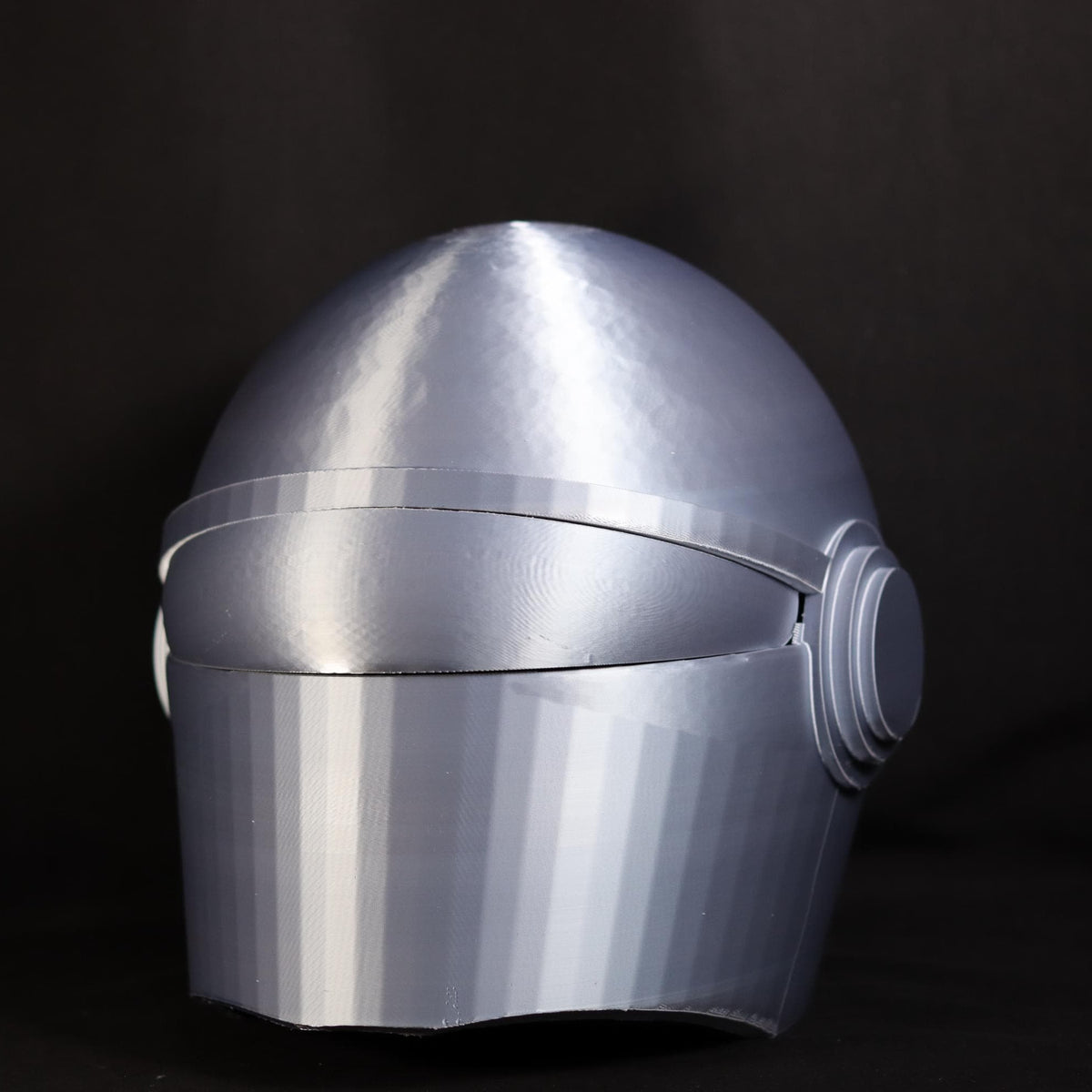 A metallic silver futuristic helmet with a smooth, rounded dome and visor, shown against a dark black background.