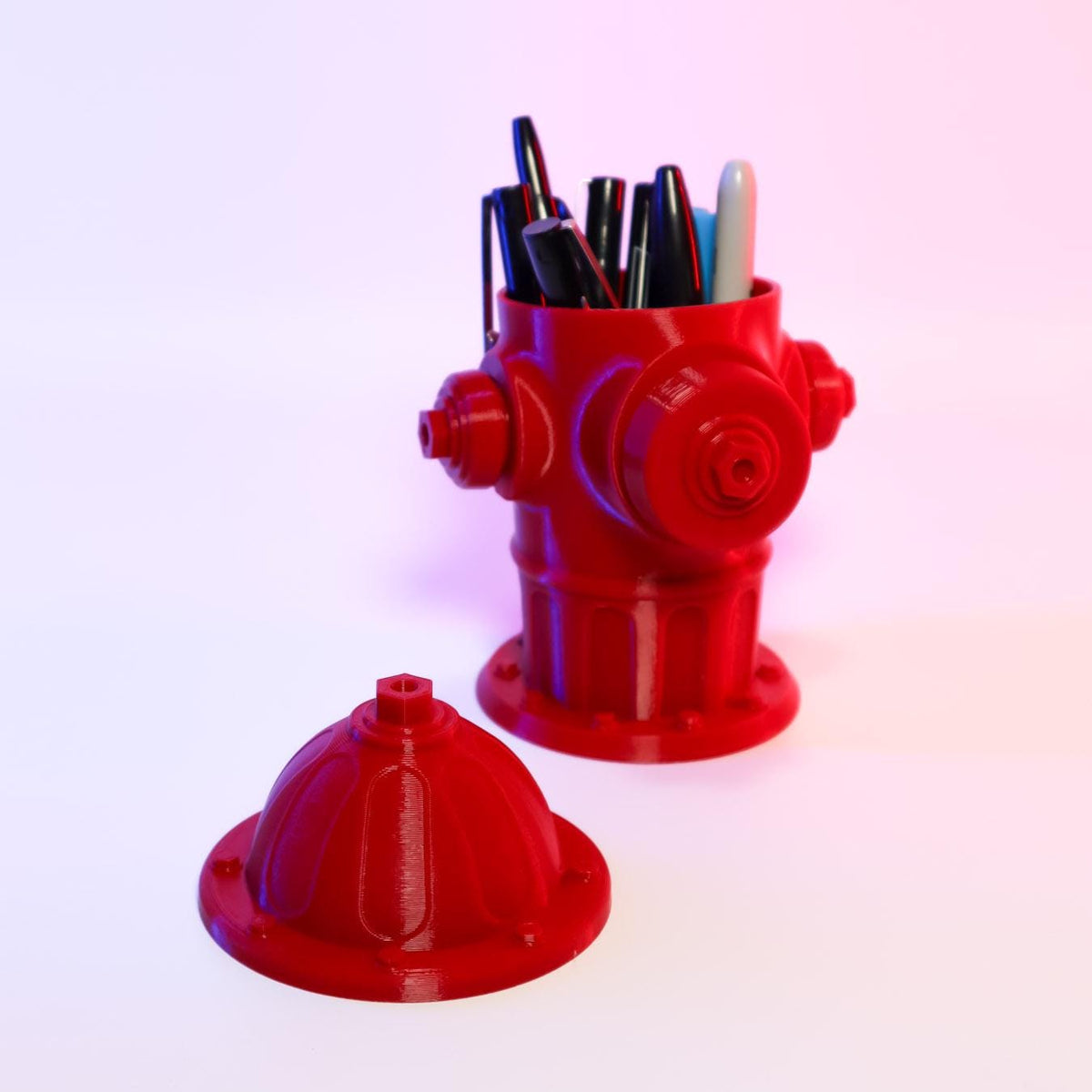 A red cartoonish mini fire hydrant 3D printed desk accessory, with its lid removed showing that it is used for holding small items like pens.